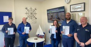 Group of students proudly holding their RYA First Aid certificates, smiling after successfully completing the course, with an instructor congratulating them in classroom environment.